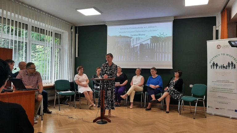 zdjęcie przedstawia Panią mówiącą przez mikrofon wraz z innymi osobami uczestniczącymi w Konferencji