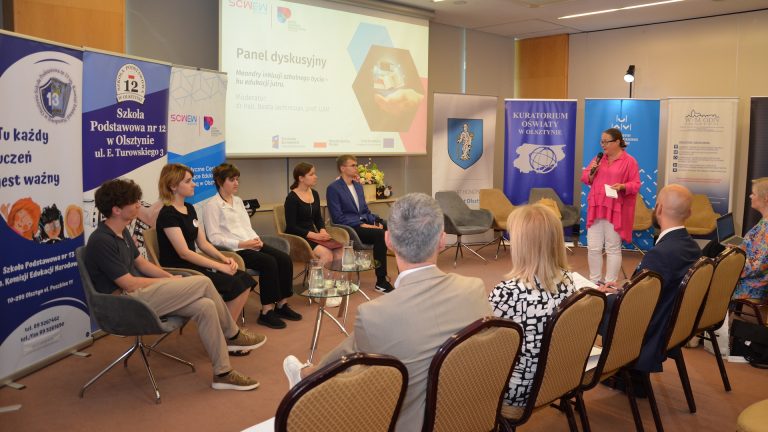 zdjęcie przedstawia osoby uczestniczące w panelu dyskusyjnym na tle roll-up