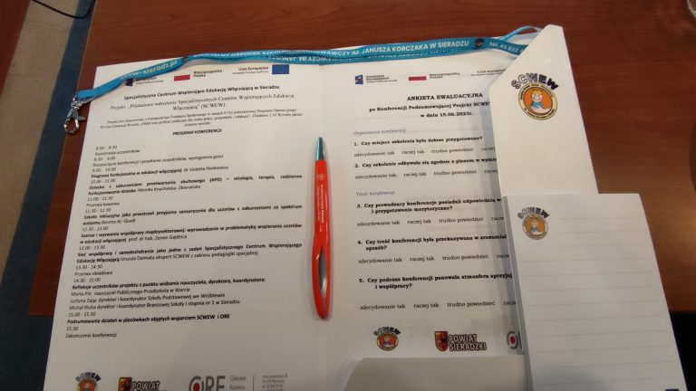 zdjęcie przedstawia komplet materiałów konferencyjnych, który dostawali uczestnicy konferencji w Sieradzu. W skład kompletu wchodzi tecz, program konferencji, długopis, notes i smycz na identyfikator.