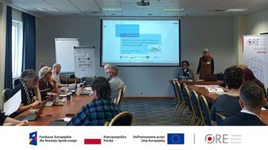 na zdjęciu sala, w której siedzą uczestnicy spotkania, Anna Pregler główny ekspert merytoryczny mówi do zebranych, w tle ekran z wyświetloną prezentacją.